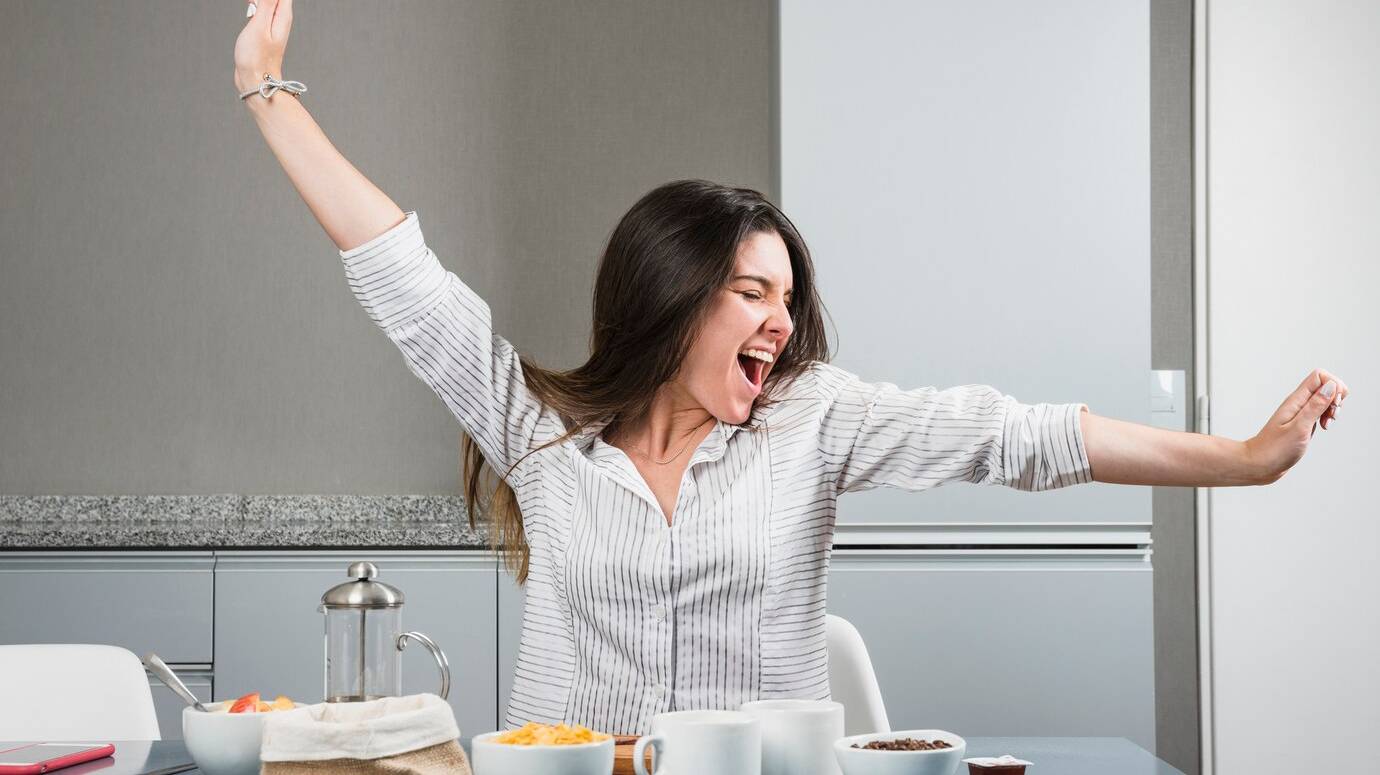 portrait-young-woman-sitting-breakfast-table-stretching-her-arms_23-2148161222