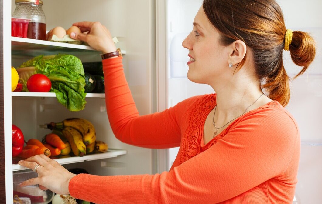 женщина складывает продукты в холодильник